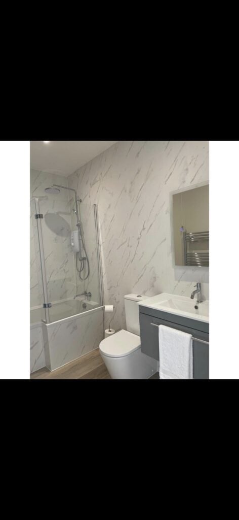 Commercial washroom installation featuring white wall tiling, blue partition panels, wall mounted urinals and washbasins, suspended ceiling with integrated lighting and grey vinyl flooring