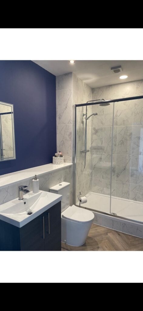 Renovated commercial washroom featuring white wall tiles, grey speckled vinyl flooring, wall mounted twin wash basins with mirrors, urinals and a toilet cubicle with suspended ceiling and natural light from a frosted window