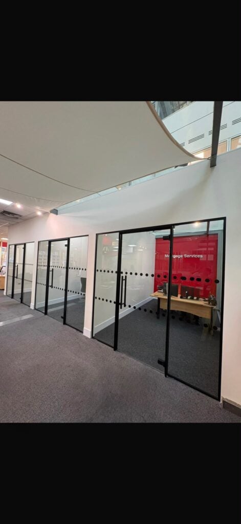 Completed commercial washroom renovation featuring white tiled walls, suspended ceiling with integrated lighting, grey vinyl flooring and modern wall mounted basins with chrome taps alongside white cubicle partitions with black hardware