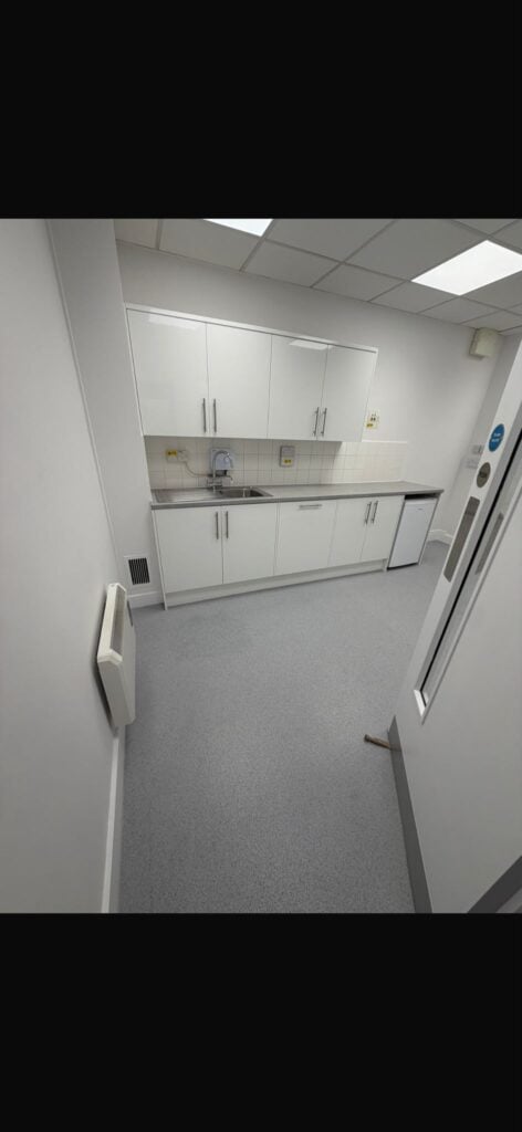 Office space marked out with blue tape on grey carpet flooring, showing workspace layout planning with desks and chairs positioned throughout the room